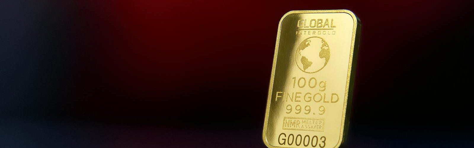 Close-up of a 100g fine gold bar against a red reflective surface, symbolizing wealth and luxury.