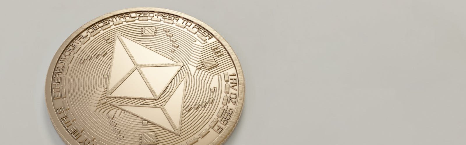 A golden Ethereum coin placed on a neutral light background, symbolizing digital currency.