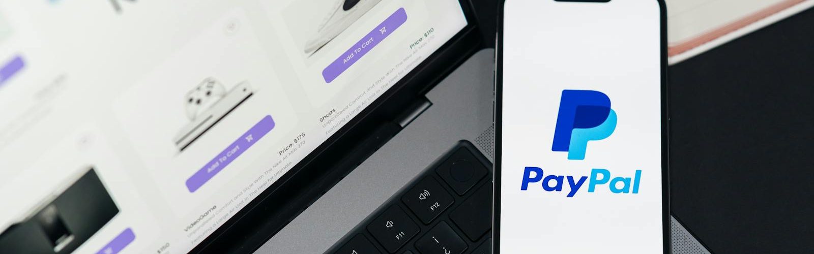 Smartphone displaying PayPal logo next to laptop with online shopping site open.