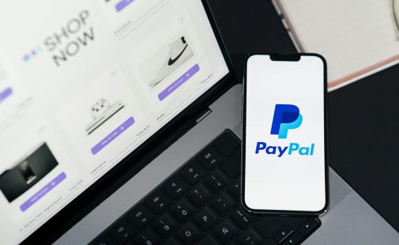 Smartphone displaying PayPal logo next to laptop with online shopping site open.