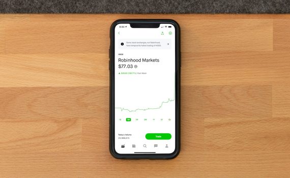 Stock trading app on smartphone displaying Robinhood Markets price on wooden desk.