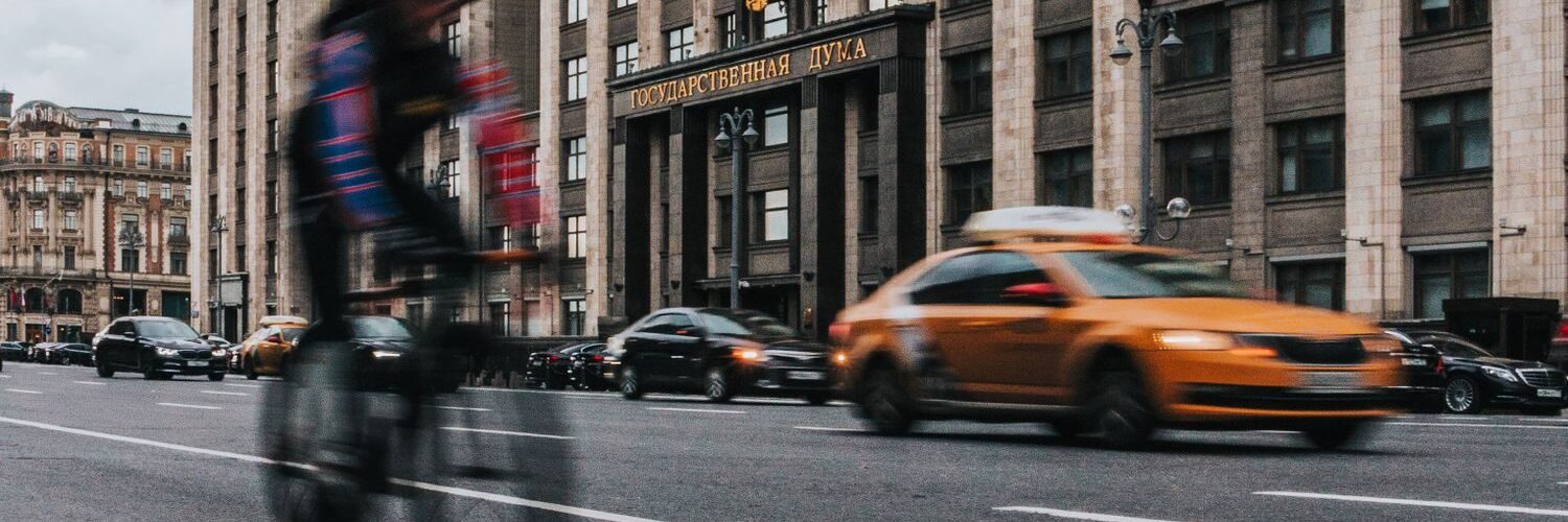 Motion blur captures a cyclist passing by traffic in front of a grand building.