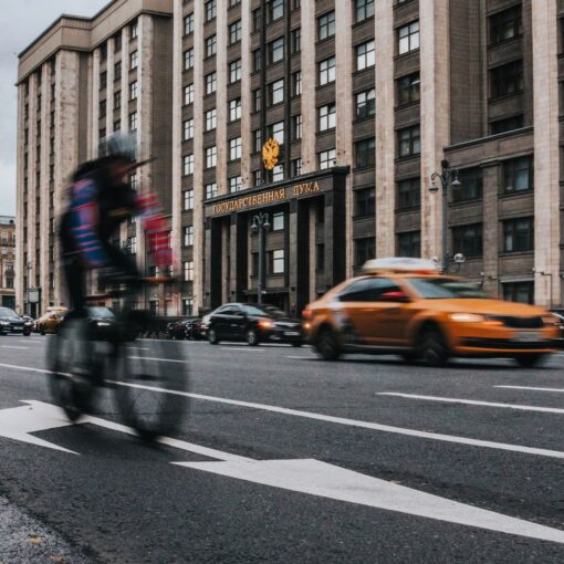 Motion blur captures a cyclist passing by traffic in front of a grand building.