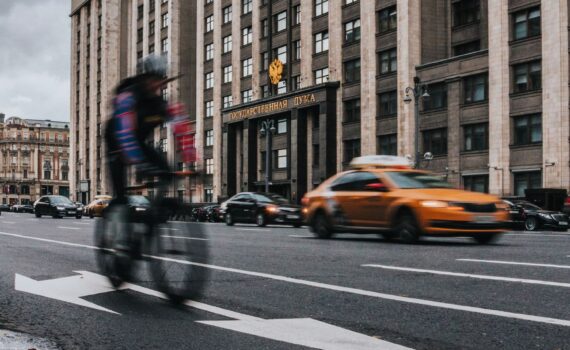 Motion blur captures a cyclist passing by traffic in front of a grand building.